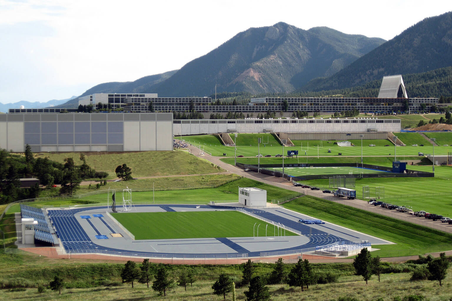 Aerial view of athletic complex with blue track, stadium, and chapel against mountain range