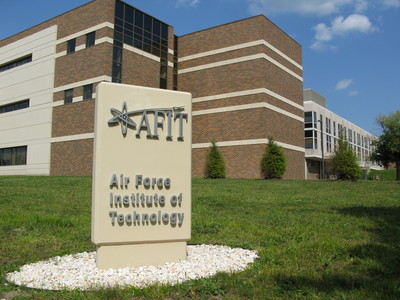 AFIT entrance sign in front of multi-story brick academic building on green lawn