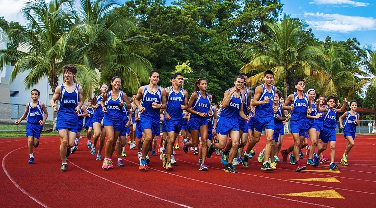 Track team in blue AMA uniforms running on red track surrounded by palm trees in Puerto Rico