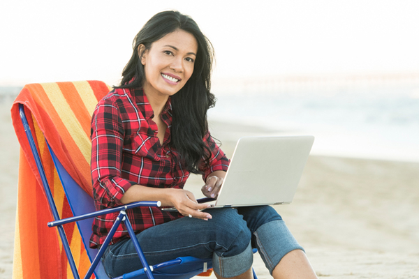 Woman studying on laptop from beach chair demonstrating flexible online learning