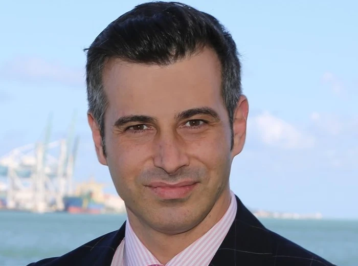 AMU faculty member in professional attire with harbor and shipping port in background