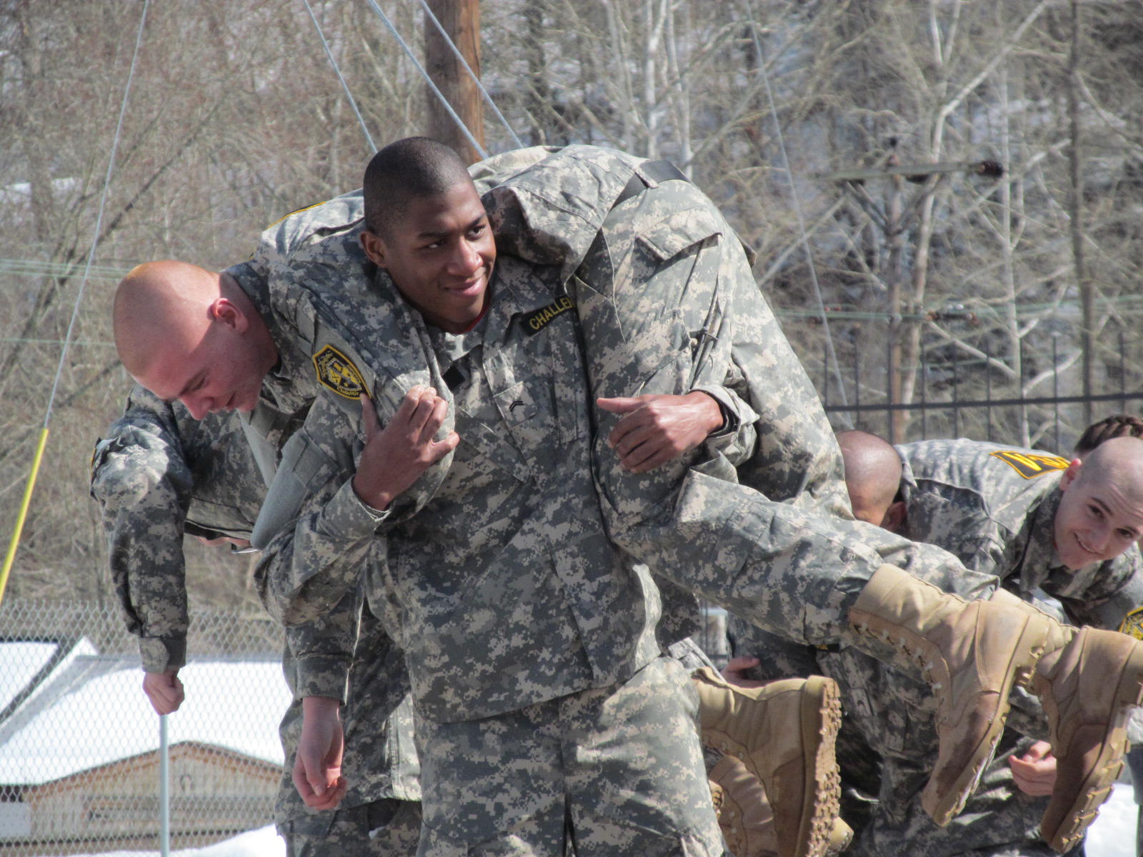 Smiling cadet carrying teammate on back during buddy carry PT exercise in winter snow