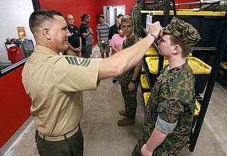 Marine instructor in khaki uniform adjusting cadet's cover during uniform inspection in equipment room