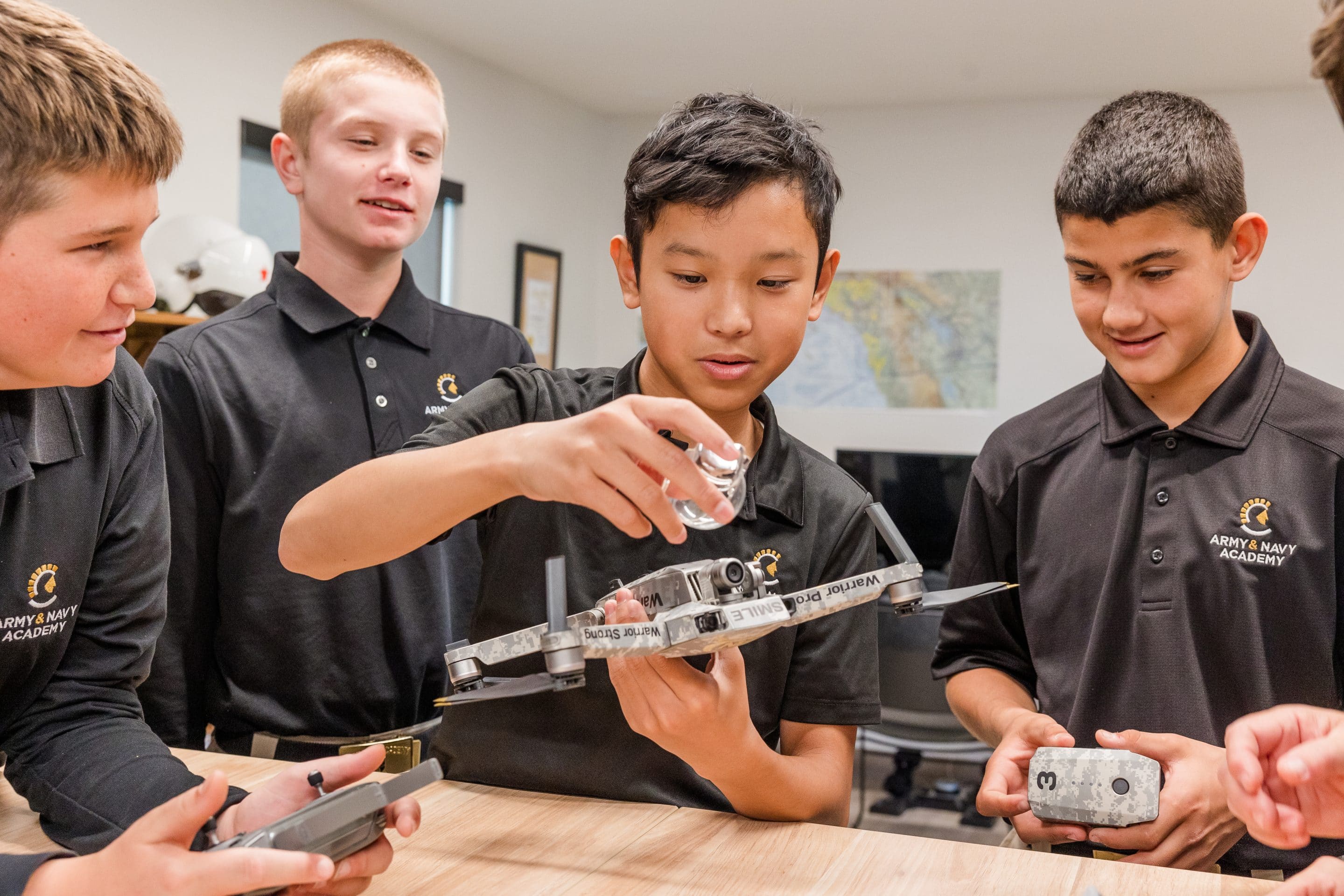 Four cadets in black polo shirts examining a drone during hands-on STEM class