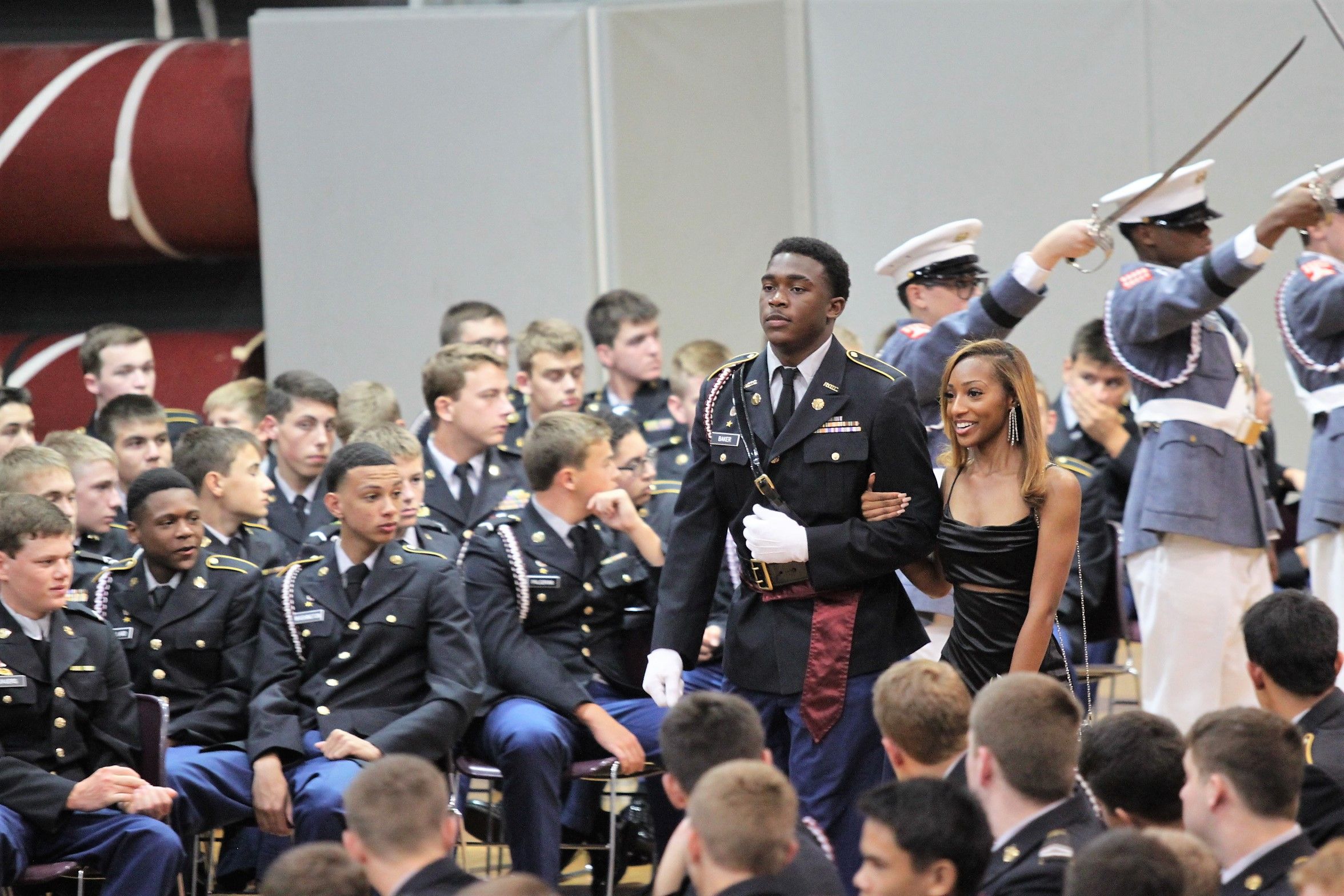 Cadet in dress uniform escorting date under raised saber arch at military ball ceremony