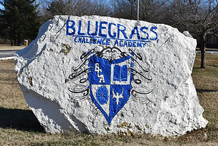 Large white painted rock entrance sign displaying Bluegrass Challenge Academy name and crest