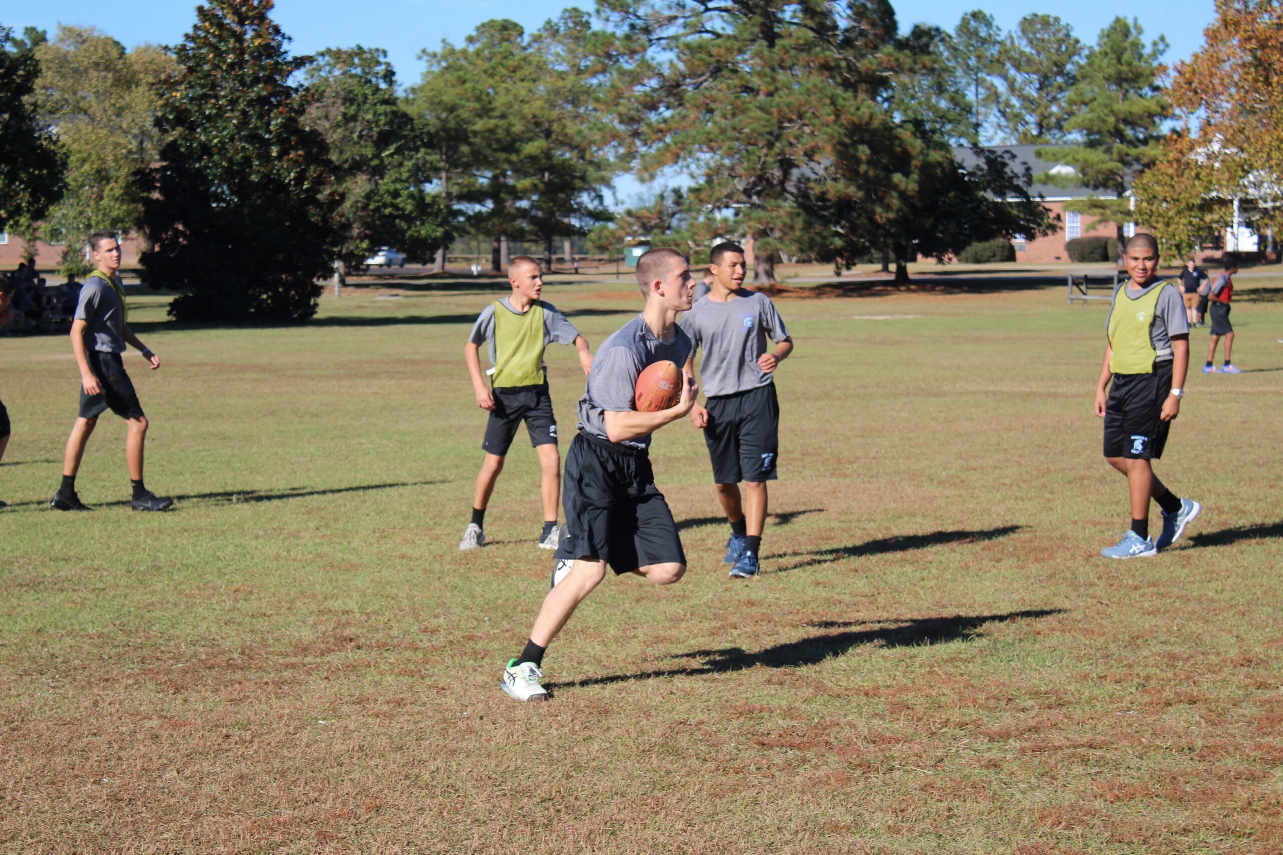 Cadets in gray PT shirts playing intramural football on grass field during afternoon recreation