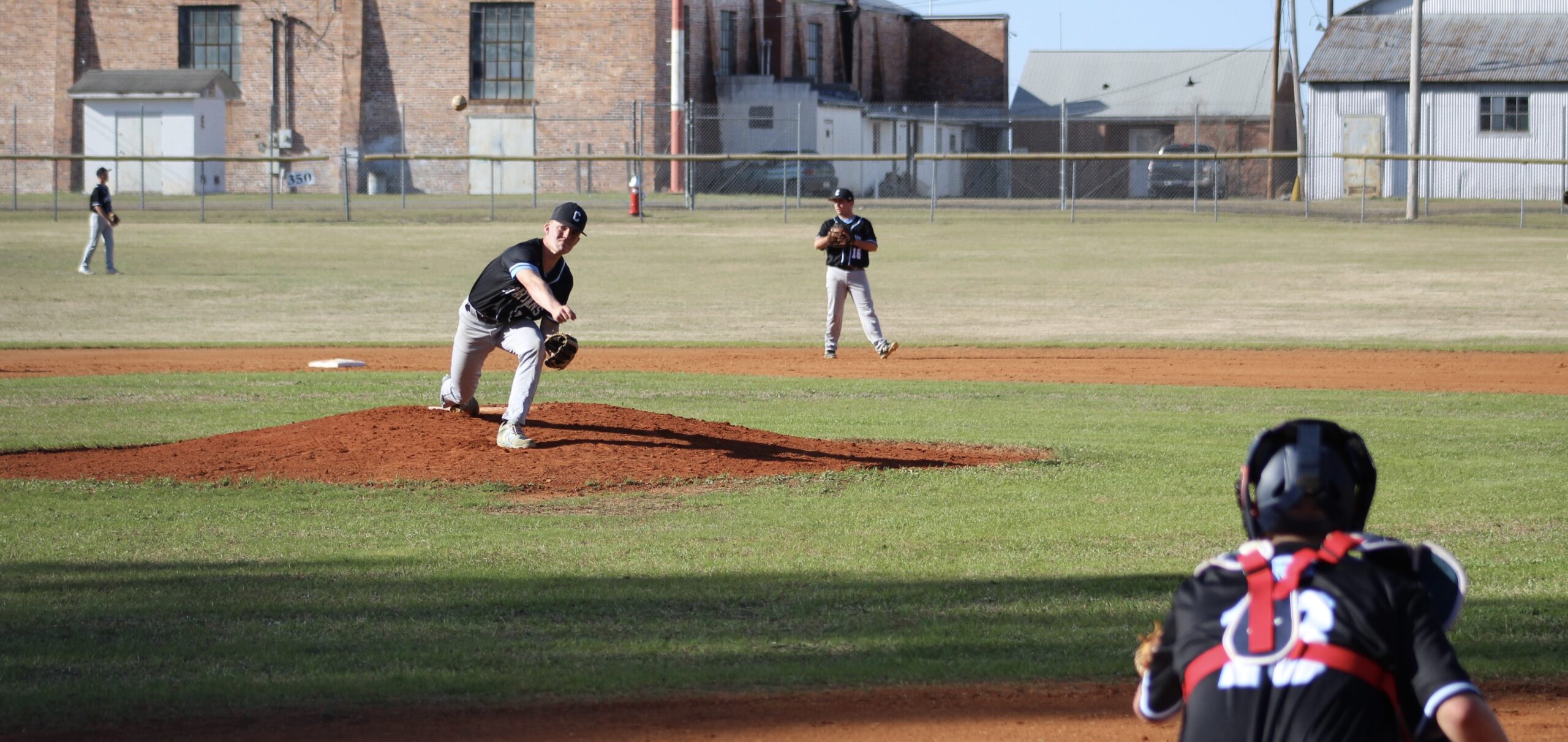 Baseball pitcher in black uniform winding up on mound with brick buildings in background