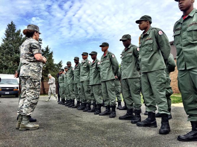 Cadets in olive green uniforms standing at attention during outdoor drill with National Guard instructor