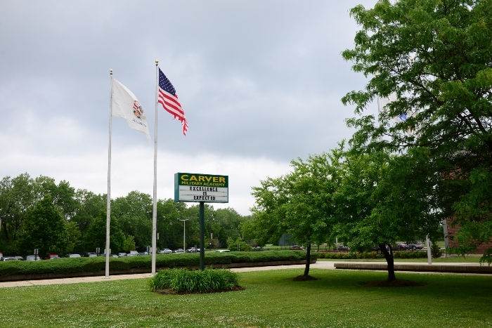 Campus entrance with American and Illinois flags, school sign reading Excellence is Expected
