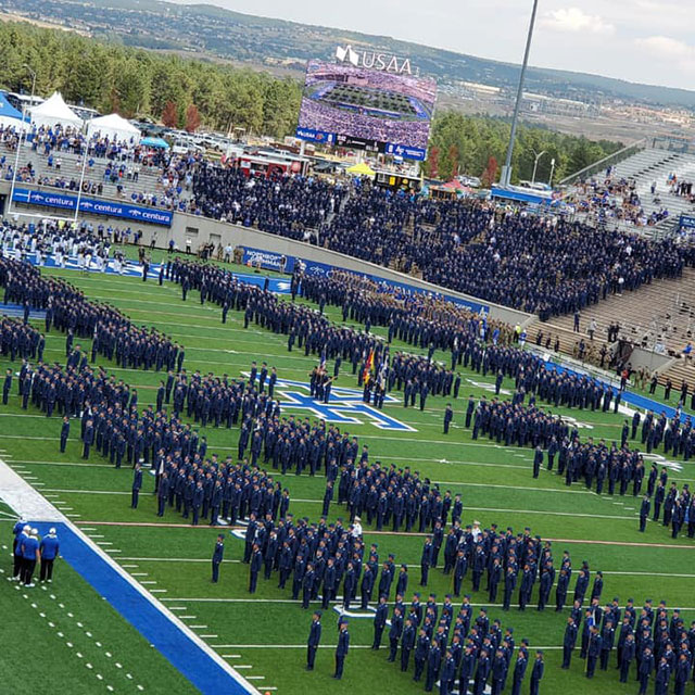Cadets in dress blue uniforms standing in formation on stadium field during ceremony