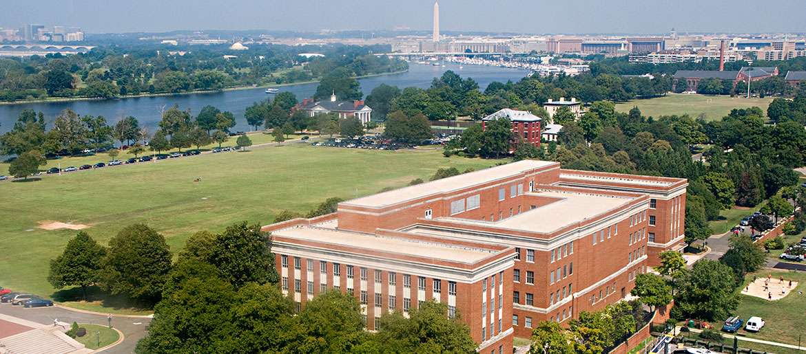 Aerial view of Fort McNair brick building with green lawns, Potomac River and Washington Monument in background