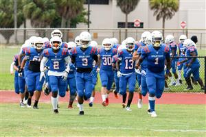 Football team in blue jerseys and helmets running onto field with palm trees in background