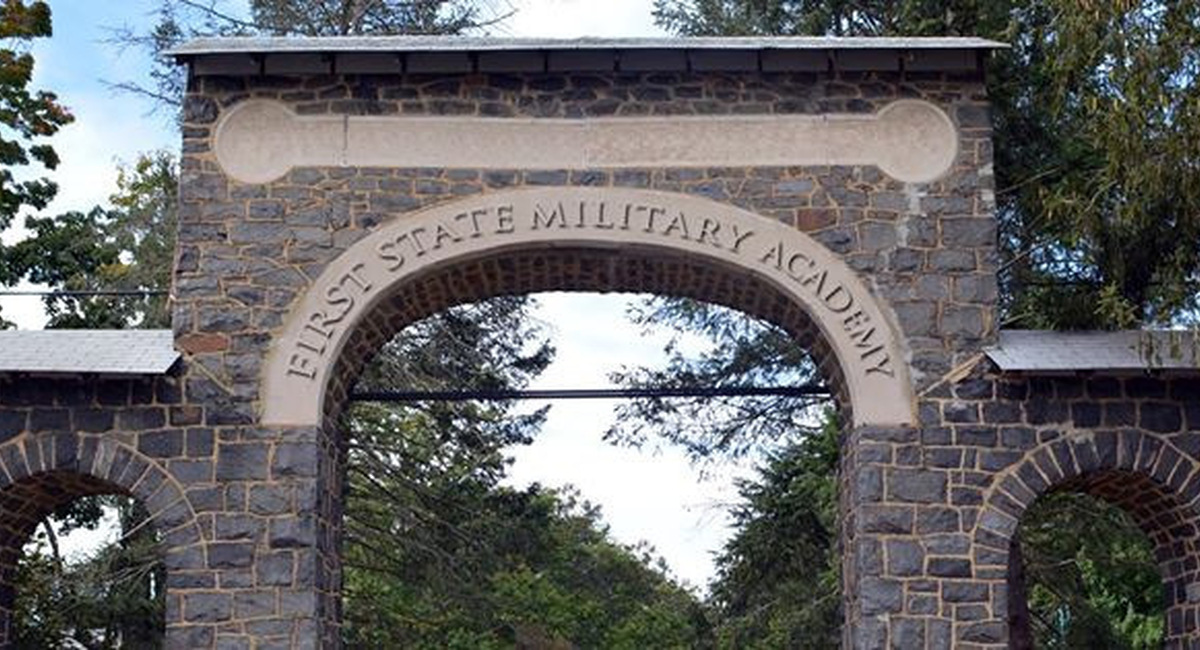Historic stone entry arch inscribed with First State Military Academy surrounded by mature trees