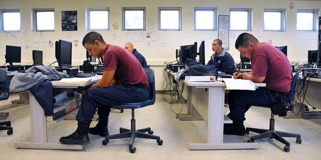 Male cadets in maroon and navy shirts working at computer workstations in bright classroom