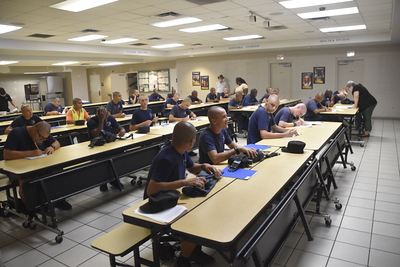 Cadets in navy blue uniforms seated at long tables during training session in classroom