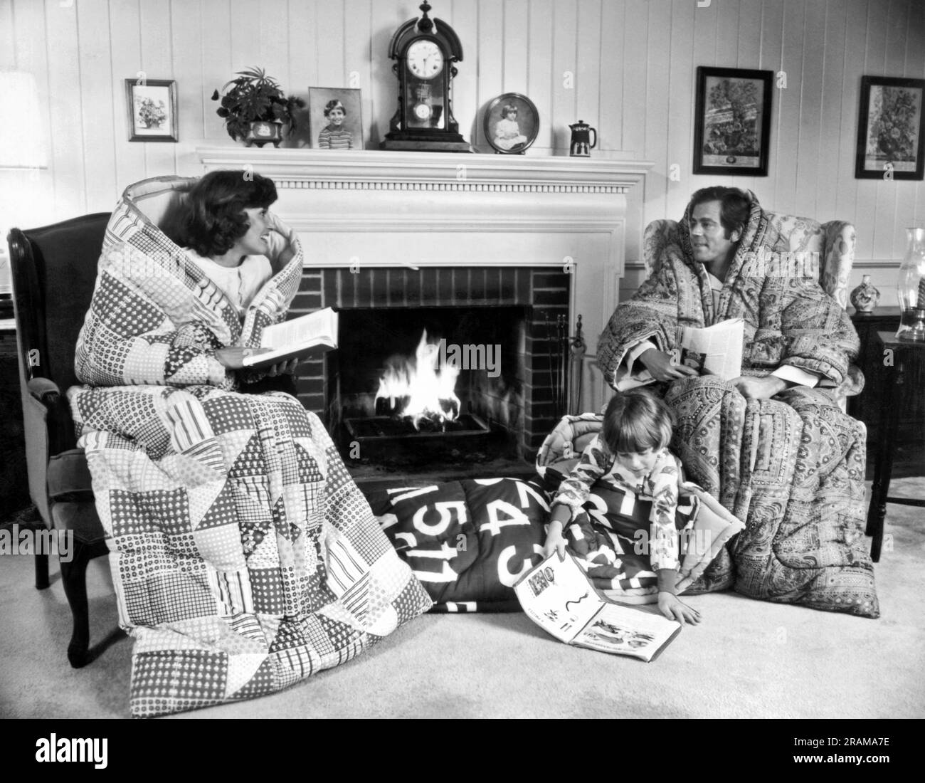 Vintage black and white photo of family reading by fireplace wrapped in quilts and blankets