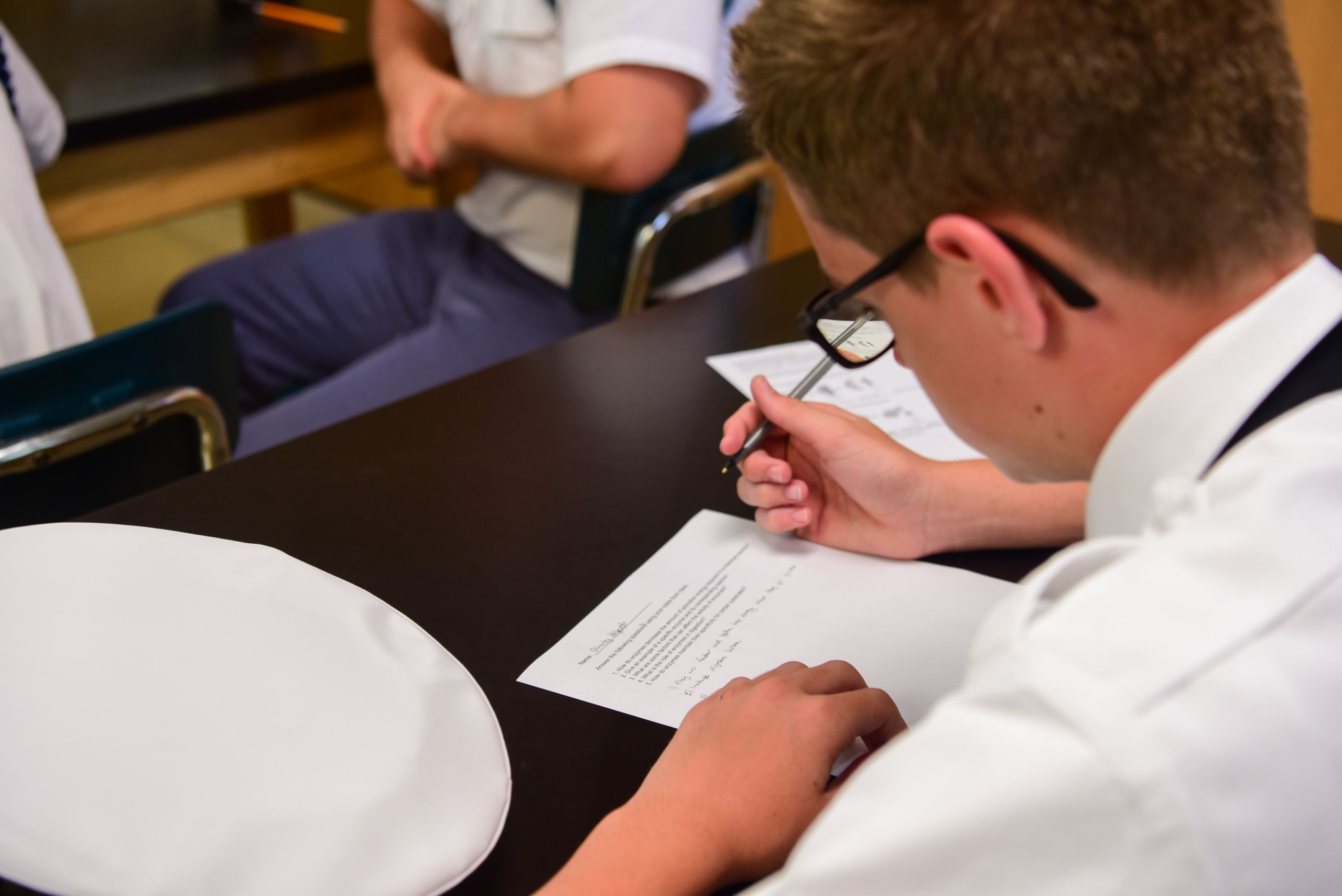 Cadet in white dress shirt and glasses completing written assignment at classroom desk