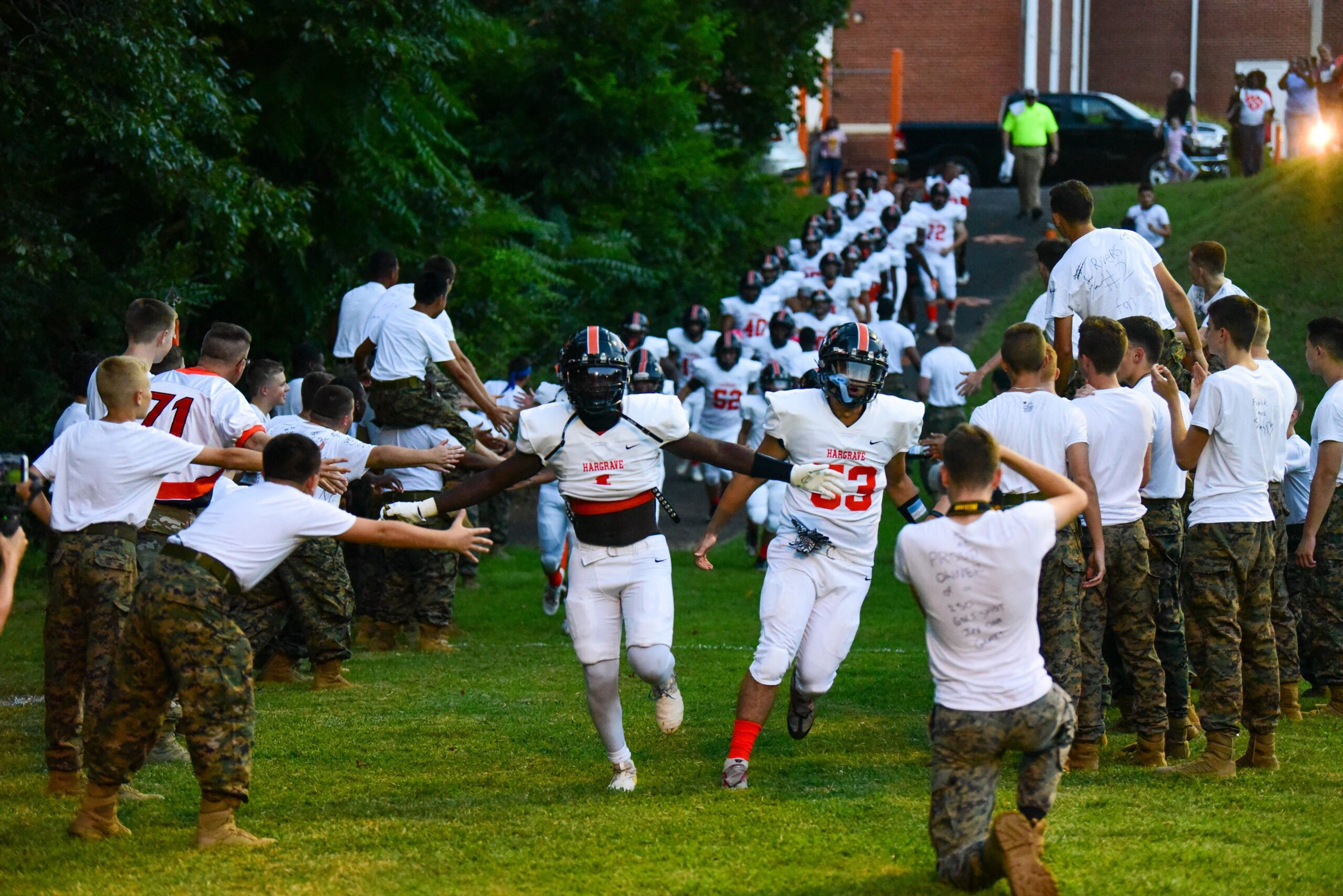 Football players in black and orange uniforms running through cadet corps honor line at dusk