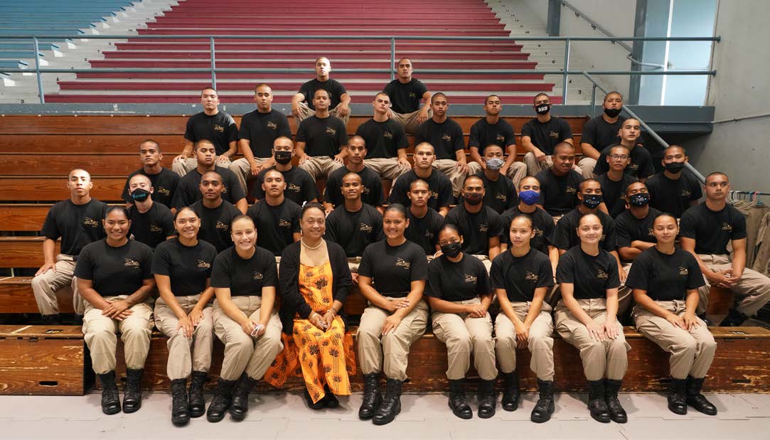 Cadet class seated on gymnasium bleachers in black t-shirts and khaki pants for group photo