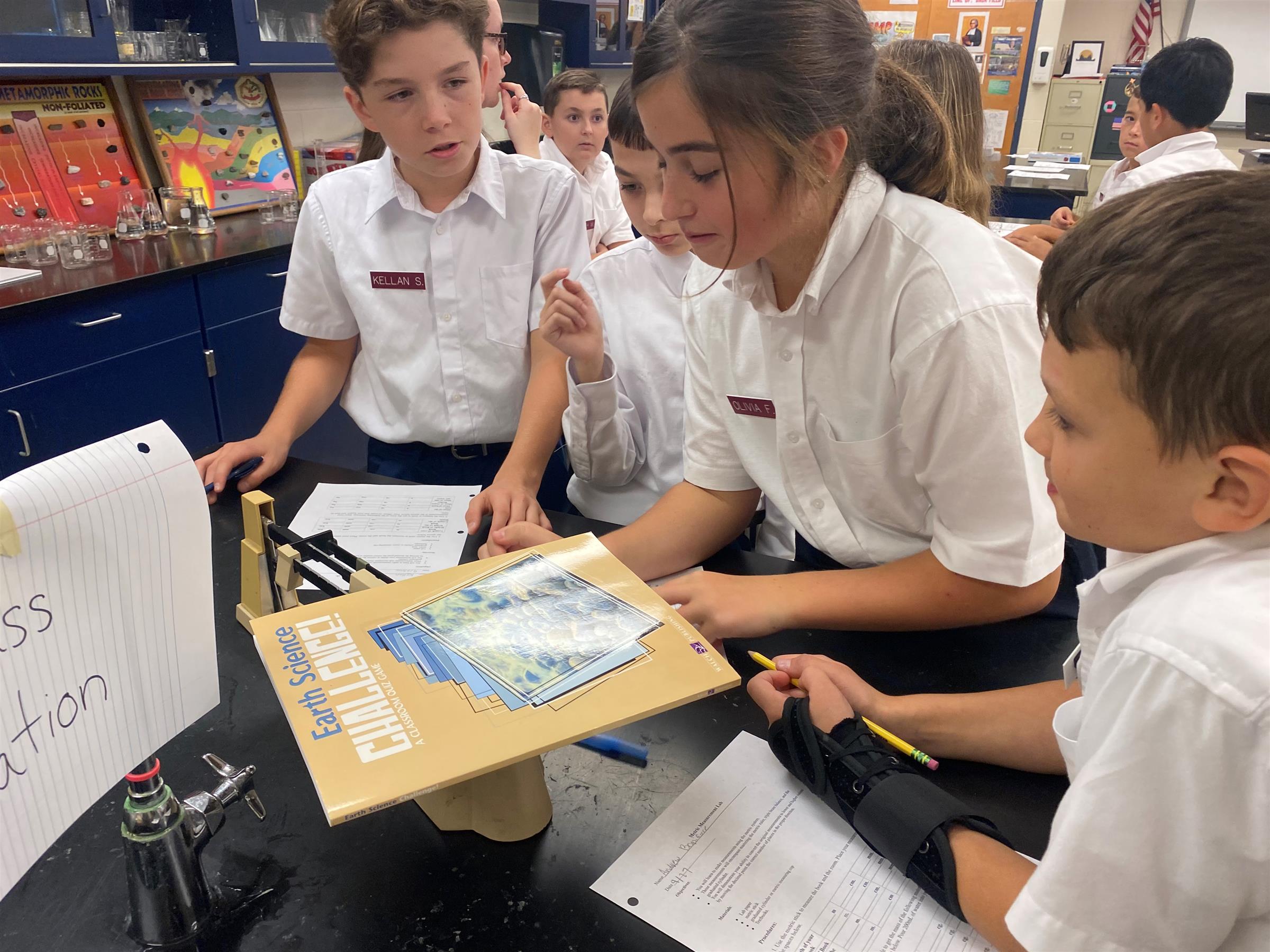 Students in white uniform shirts studying Earth Science textbook together in science laboratory