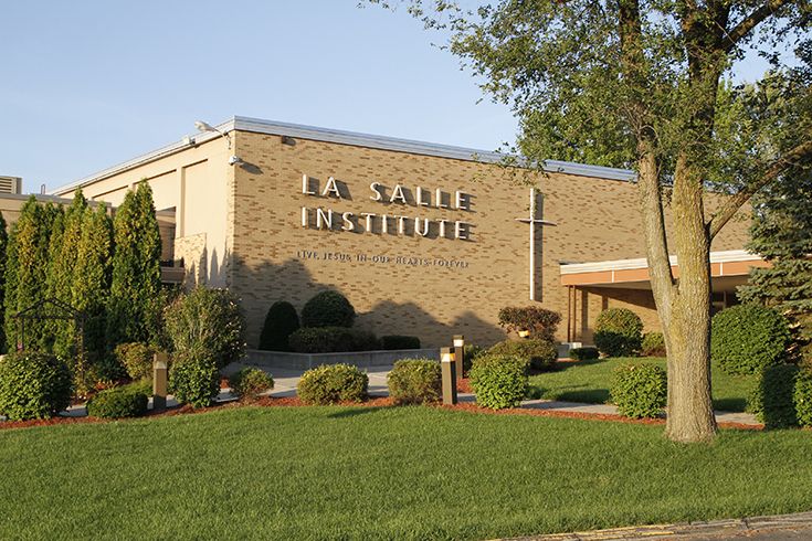 Yellow brick main building with La Salle Institute lettering, white cross, and landscaped lawn