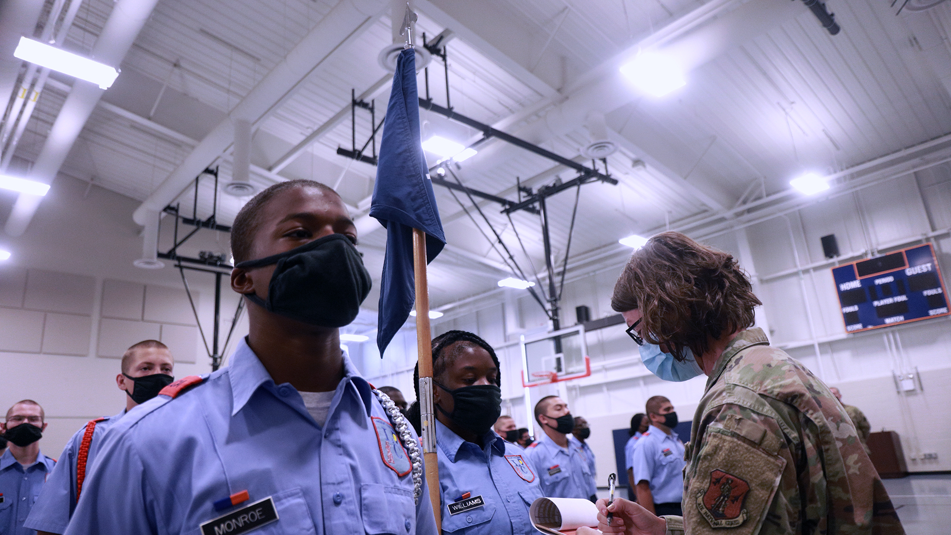 Cadets in blue uniforms receiving awards from National Guard soldier in gymnasium during ceremony