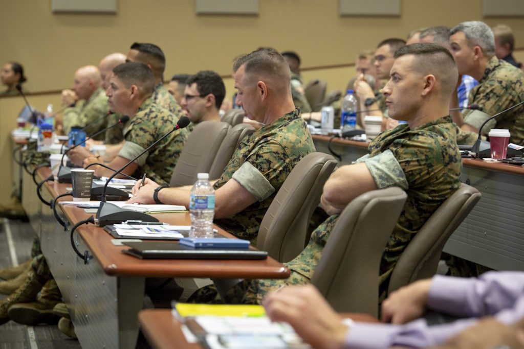 Marines in camouflage uniforms seated at conference tables during seminar lecture