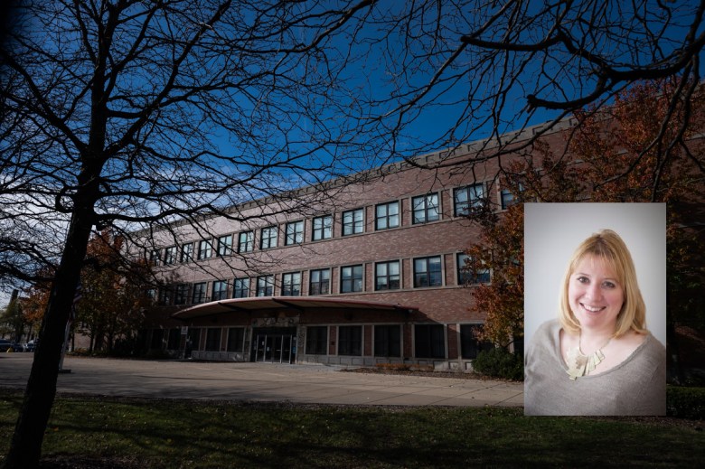 Three-story red brick school building with rows of windows framed by bare autumn trees