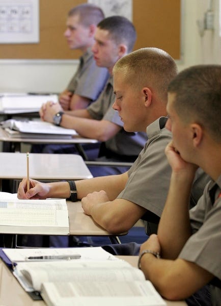 Male cadets with regulation haircuts in olive drab uniforms studying from textbooks at classroom desks