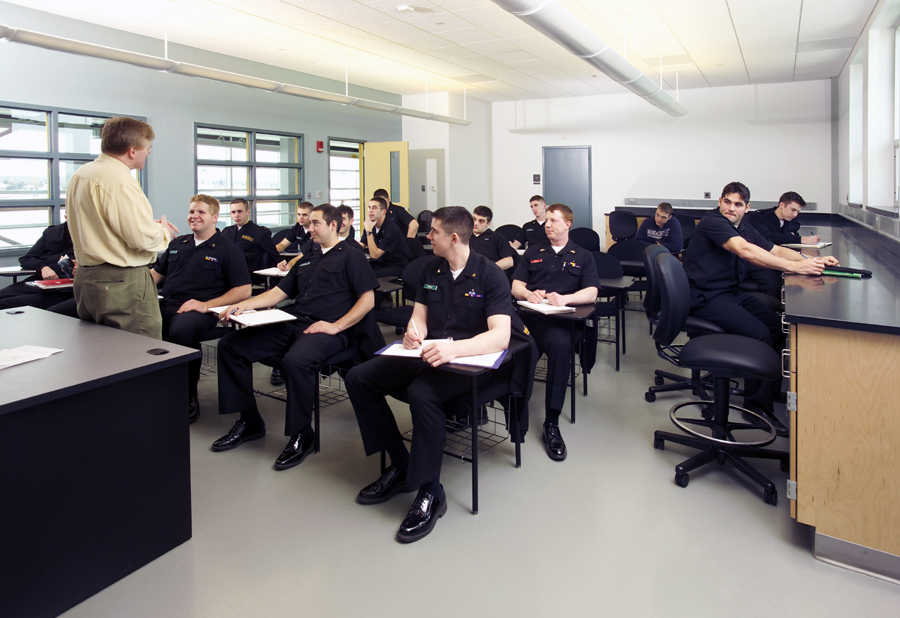 Cadets in navy blue uniforms attending lecture in modern classroom with instructor at front