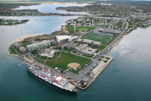 Aerial view of entire waterfront campus peninsula showing athletic fields, buildings, and training ship at dock