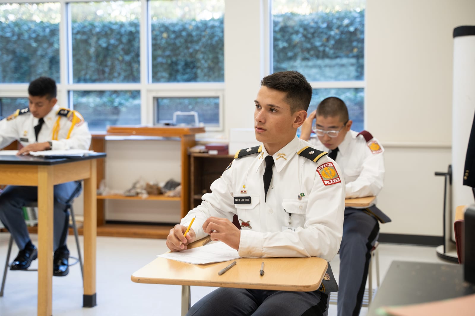 Cadets in white dress uniforms with gold epaulettes taking notes in classroom