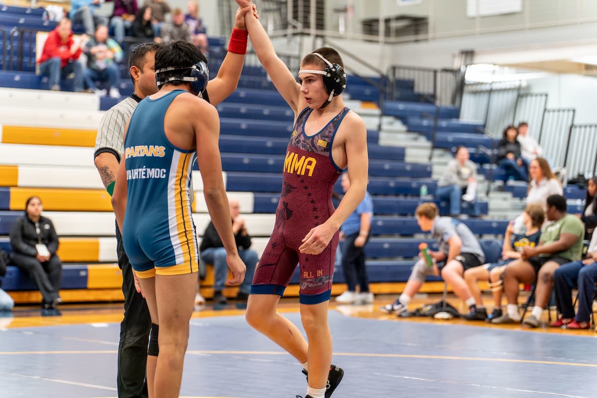 MMA wrestler in maroon singlet getting hand raised after winning match against opponent