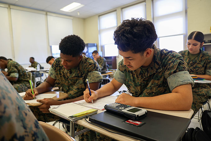 Cadets in woodland camo working on math problems with calculators in bright classroom