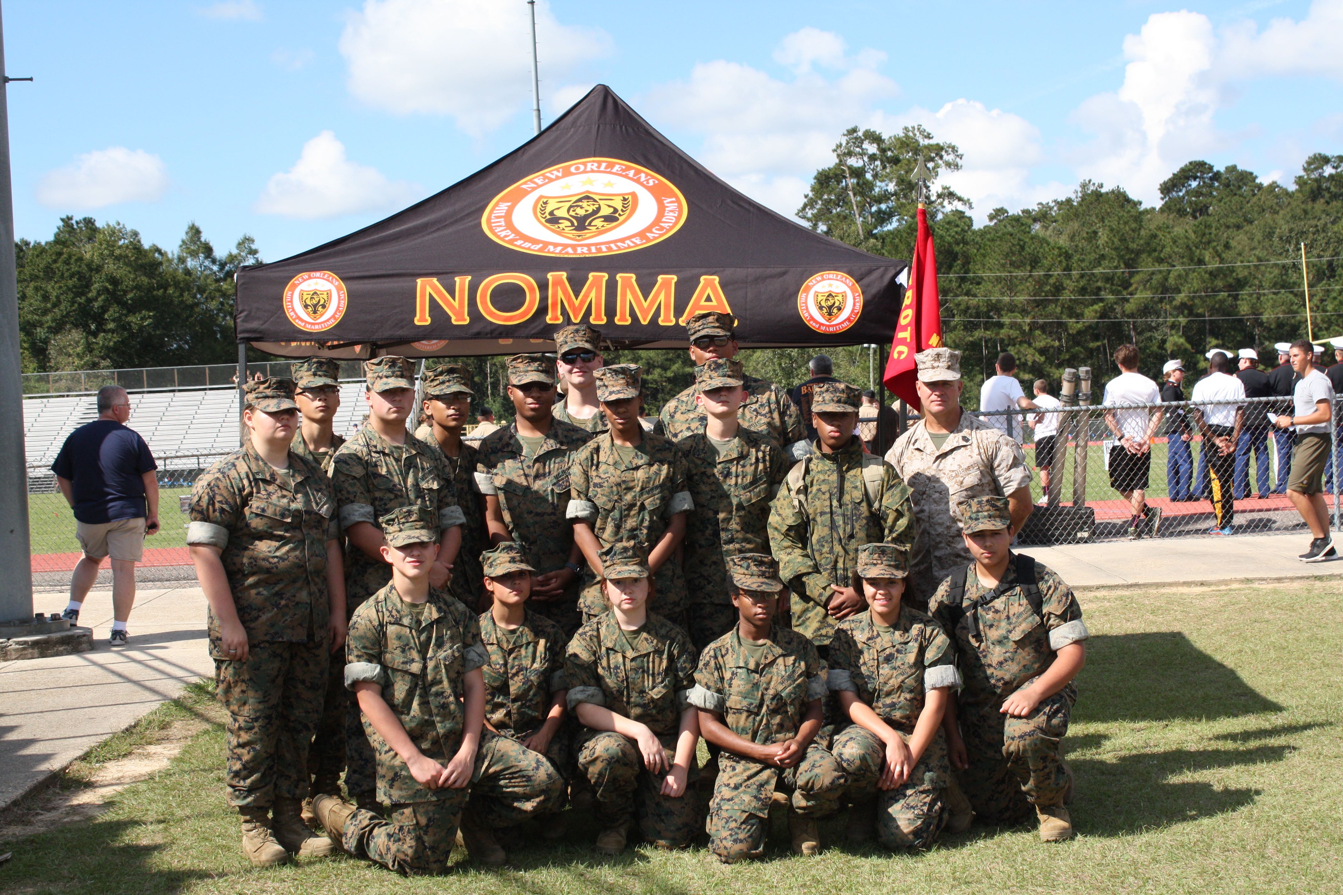 MCJROTC cadet team in woodland camo poses under NOMMA tent at outdoor athletic competition