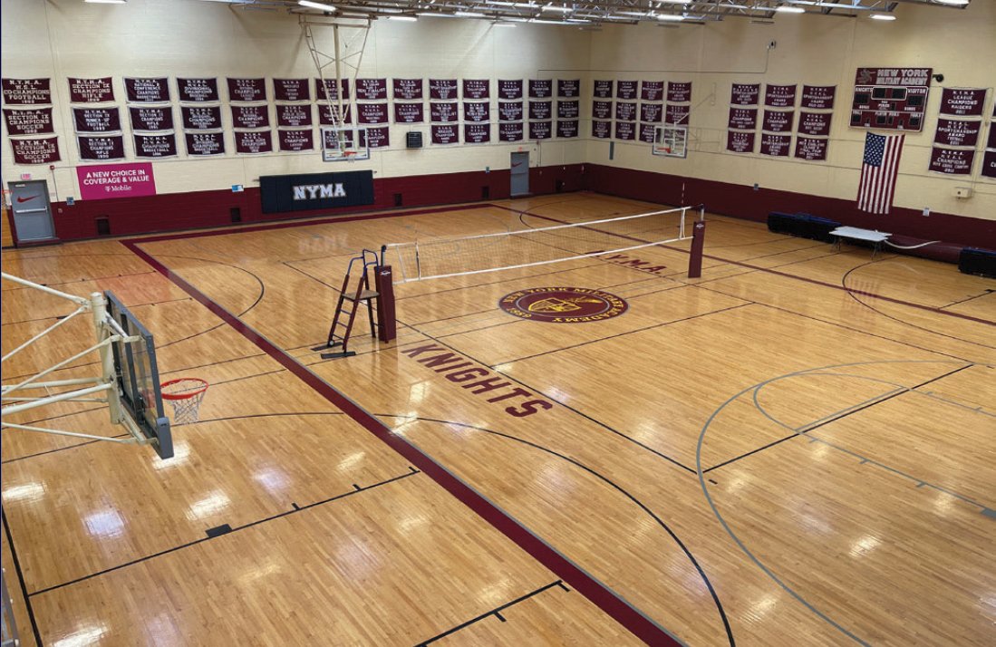 NYMA gymnasium with polished hardwood court, Knights logo at center, volleyball net, championship banners on walls