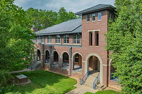 Historic three-story brick building with arched colonnade and green metal roof surrounded by trees