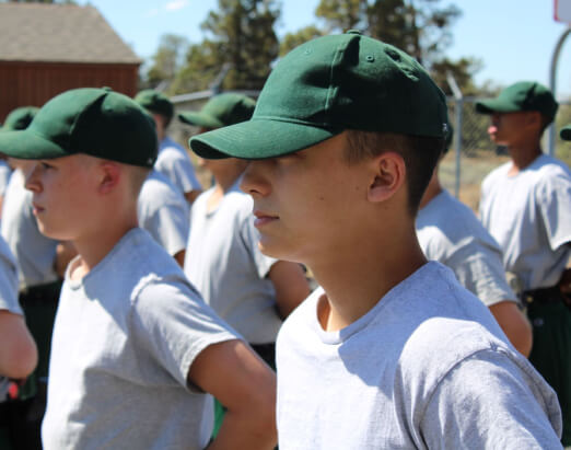 Cadets in gray t-shirts and green caps standing in formation outdoors on a sunny day in Bend, Oregon