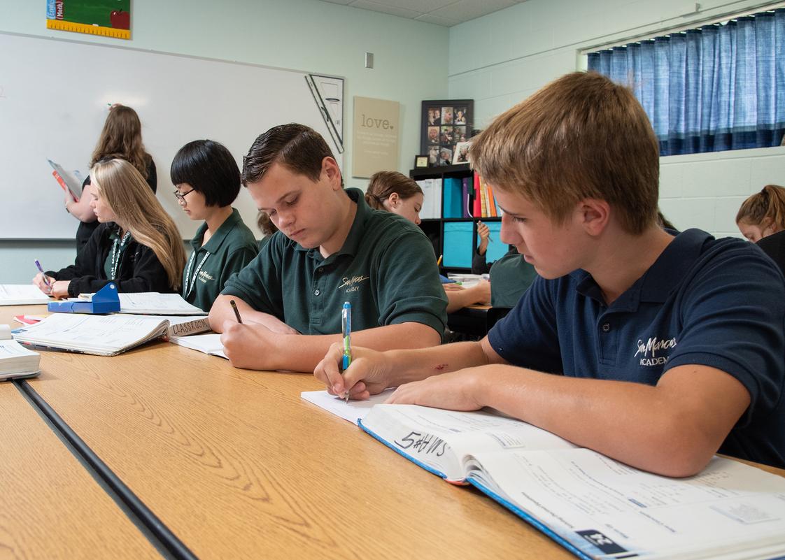 High school students in green and navy polo uniforms studying and writing at classroom desks