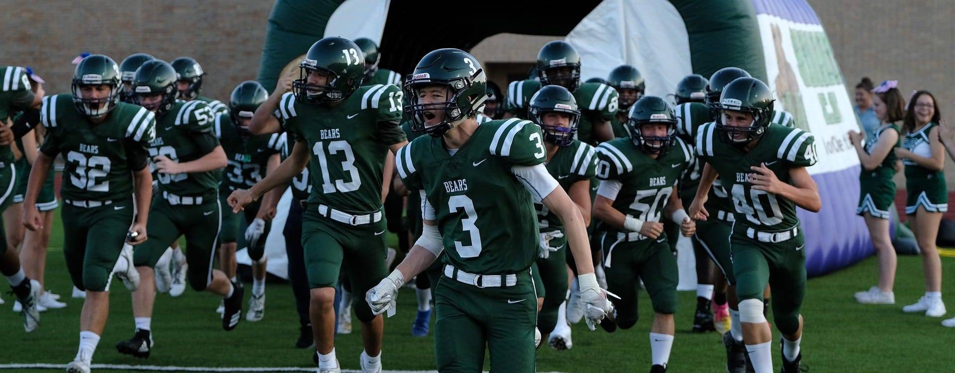 Bears football team in green uniforms running onto field through inflatable tunnel with cheerleaders
