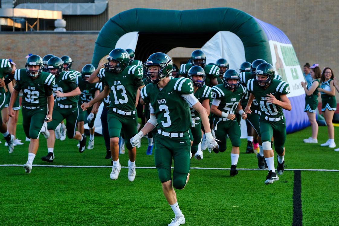 Football players in green Bears jerseys charging onto turf field led by number 3 quarterback