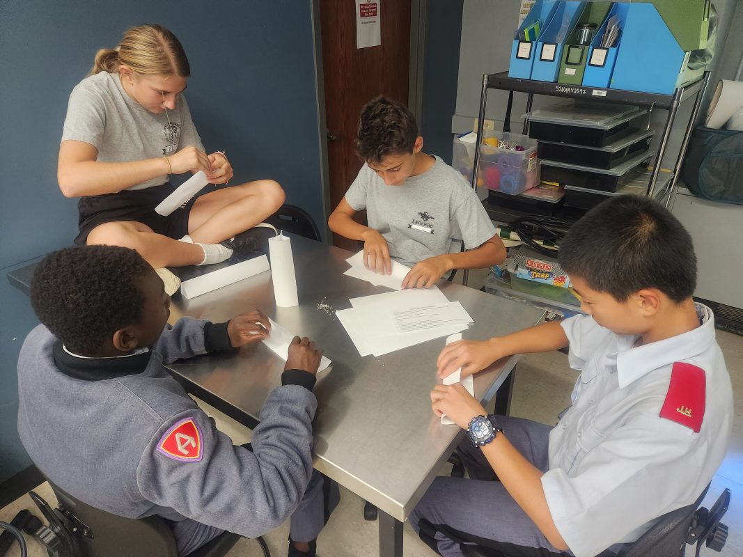 Four students in mixed uniforms collaborating on hands-on STEM project at classroom table
