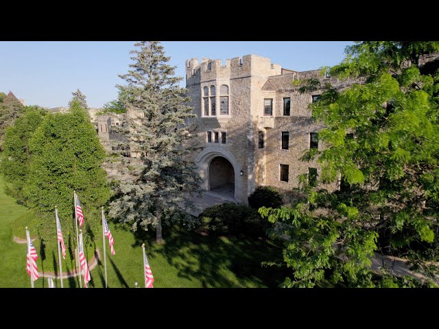 Castle-style stone administration building with arched entrance and American flags on manicured lawn