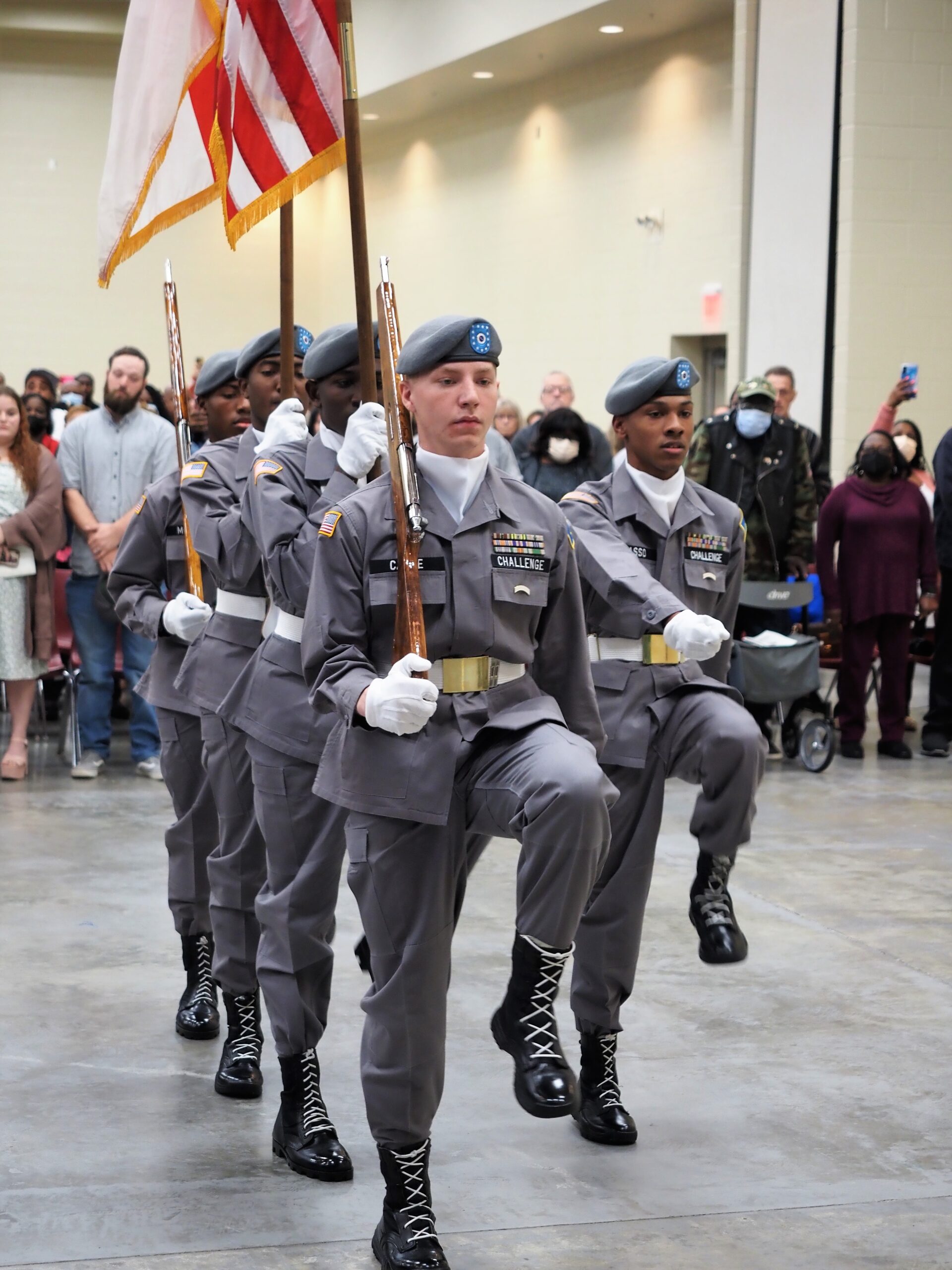 Color guard cadets in gray uniforms and berets marching with rifles and flags