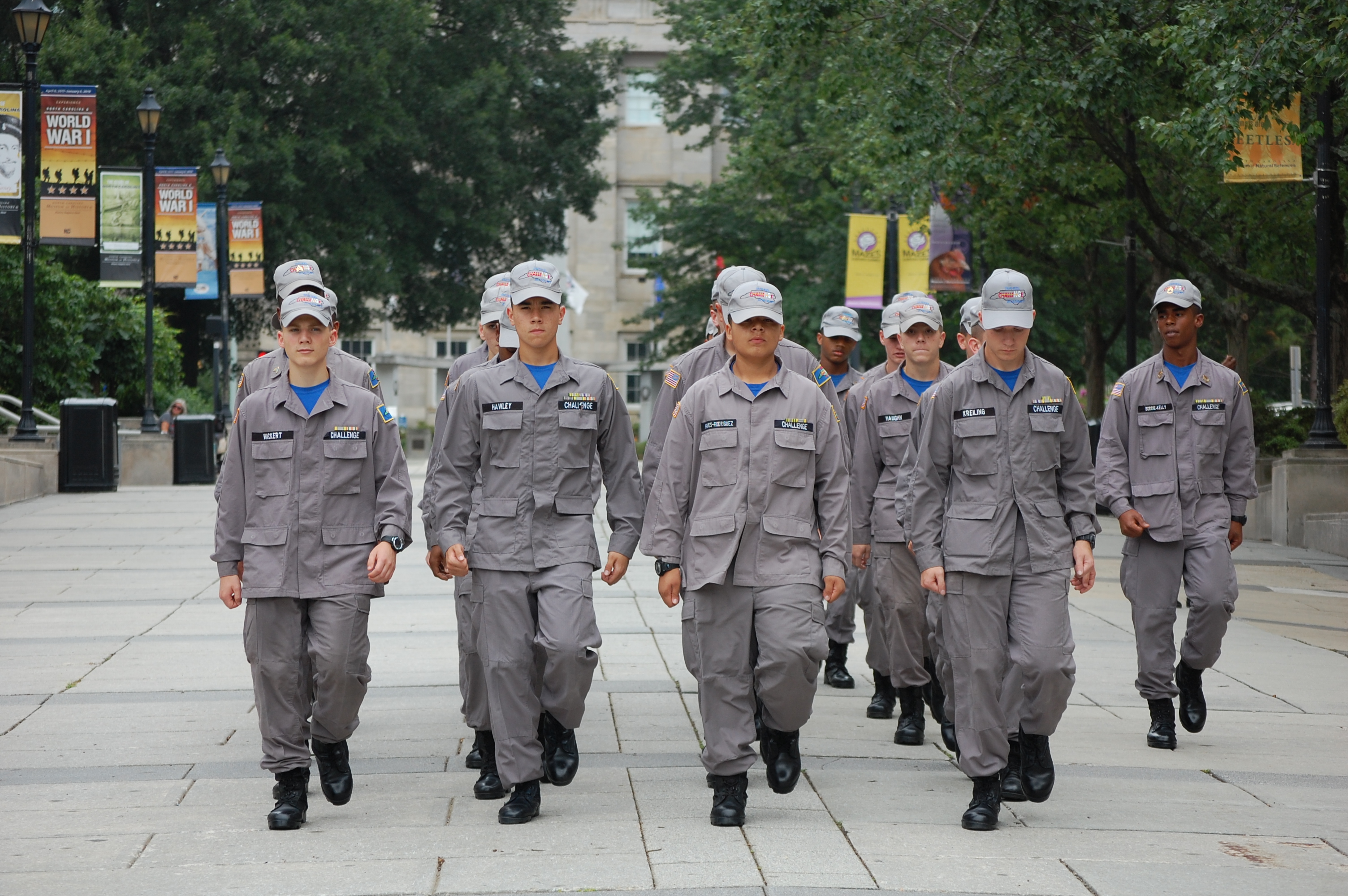 Cadets in gray uniforms and caps marching in formation through urban plaza
