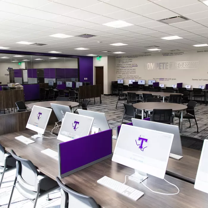 Modern computer lab with iMacs displaying Tarleton logo, round study tables, and Compete in the Classroom wall text