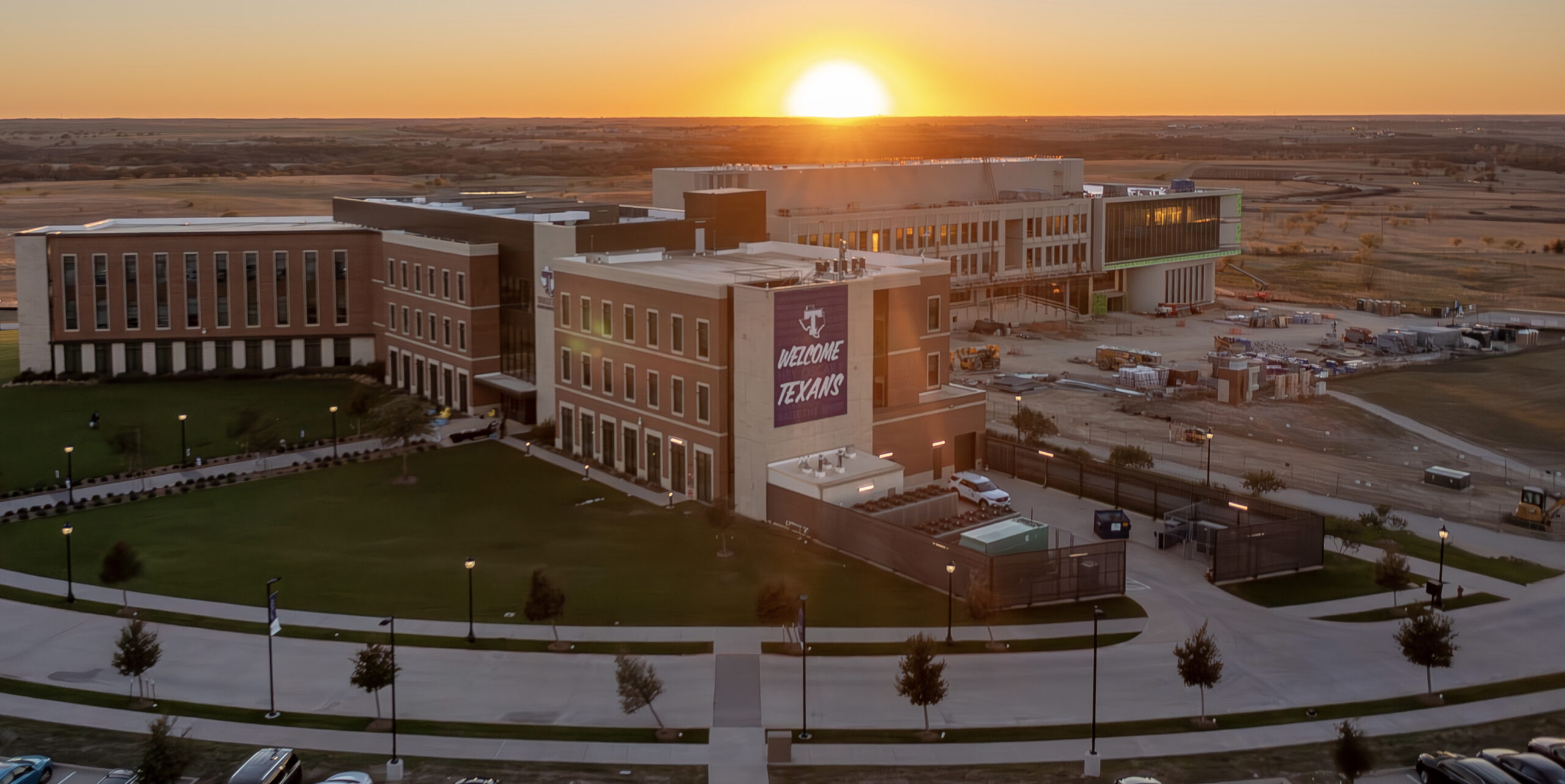 Aerial sunset view of campus buildings with Welcome Texans banner, construction site visible in background