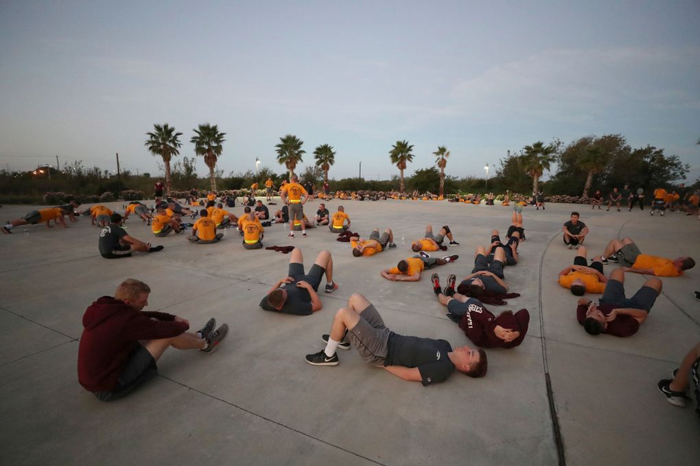 Cadets in gold and maroon PT shirts doing calisthenics outdoors at dawn with palm trees