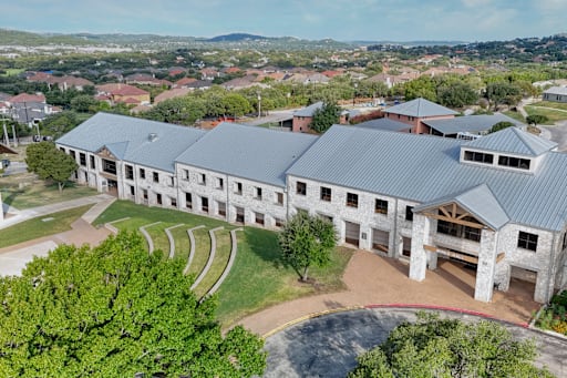 Aerial view of main academic building with gray metal roof and Texas Hill Country homes in background